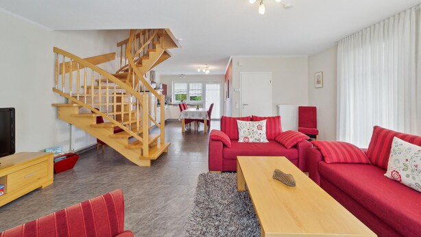 A modern living room with a wooden staircase, red sofas, a wooden coffee table, and a dining area in the background. - 3 bedroom stunning home in Haren (Ems) (Haren (Ems))