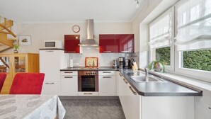 A modern kitchen with white and red cabinets, a stainless steel stove, and a large window with a view of greenery. - 3 bedroom stunning home in Haren (Ems) (Haren (Ems))