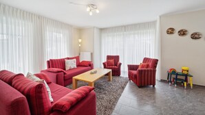 A living room with a red sofa set, a wooden coffee table, and two armchairs. There is a lamp, a small table with toys, and a wall with decorative plates. - 3 bedroom stunning home in Haren (Ems) (Haren (Ems))