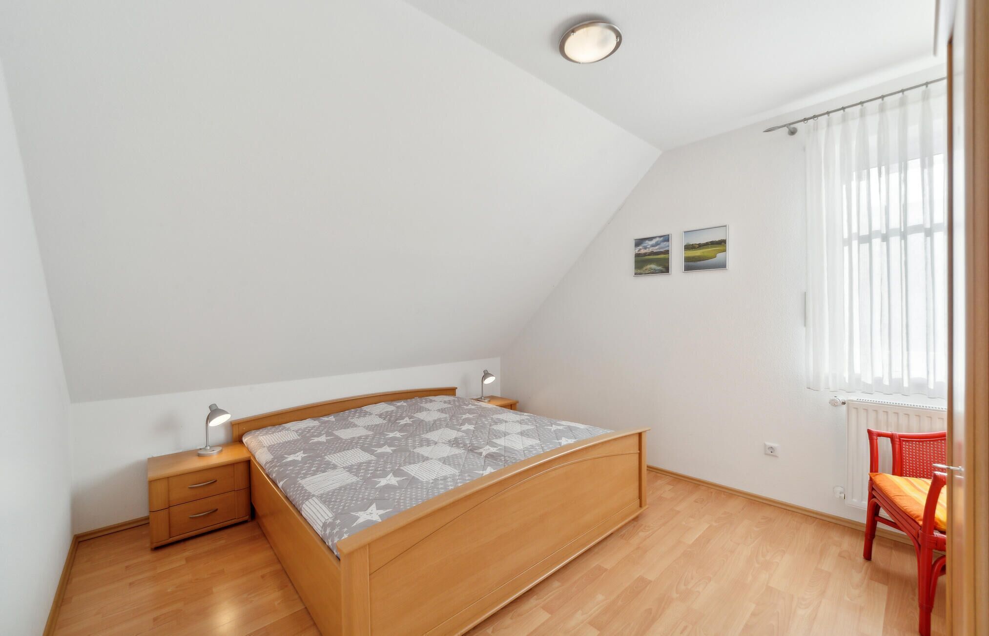 A bedroom with a wooden bed, a nightstand, a desk, a chair, and a window with curtains.