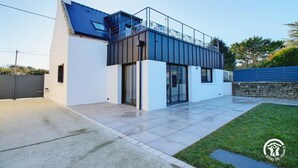 Une maison moderne à deux étages, dotée d’un balcon, d’un garage et d’un mur en pierre.