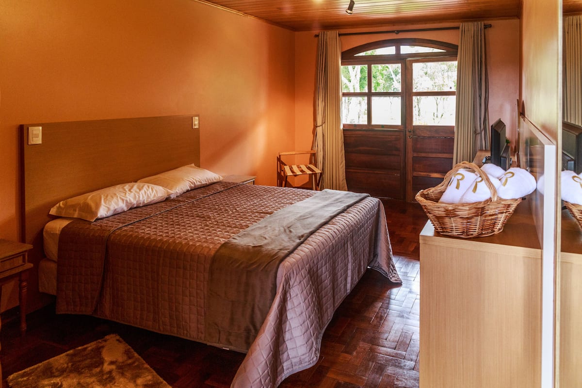 A wooden-framed bedroom with a large bed, a chair, a basket of towels, and a wooden wardrobe.