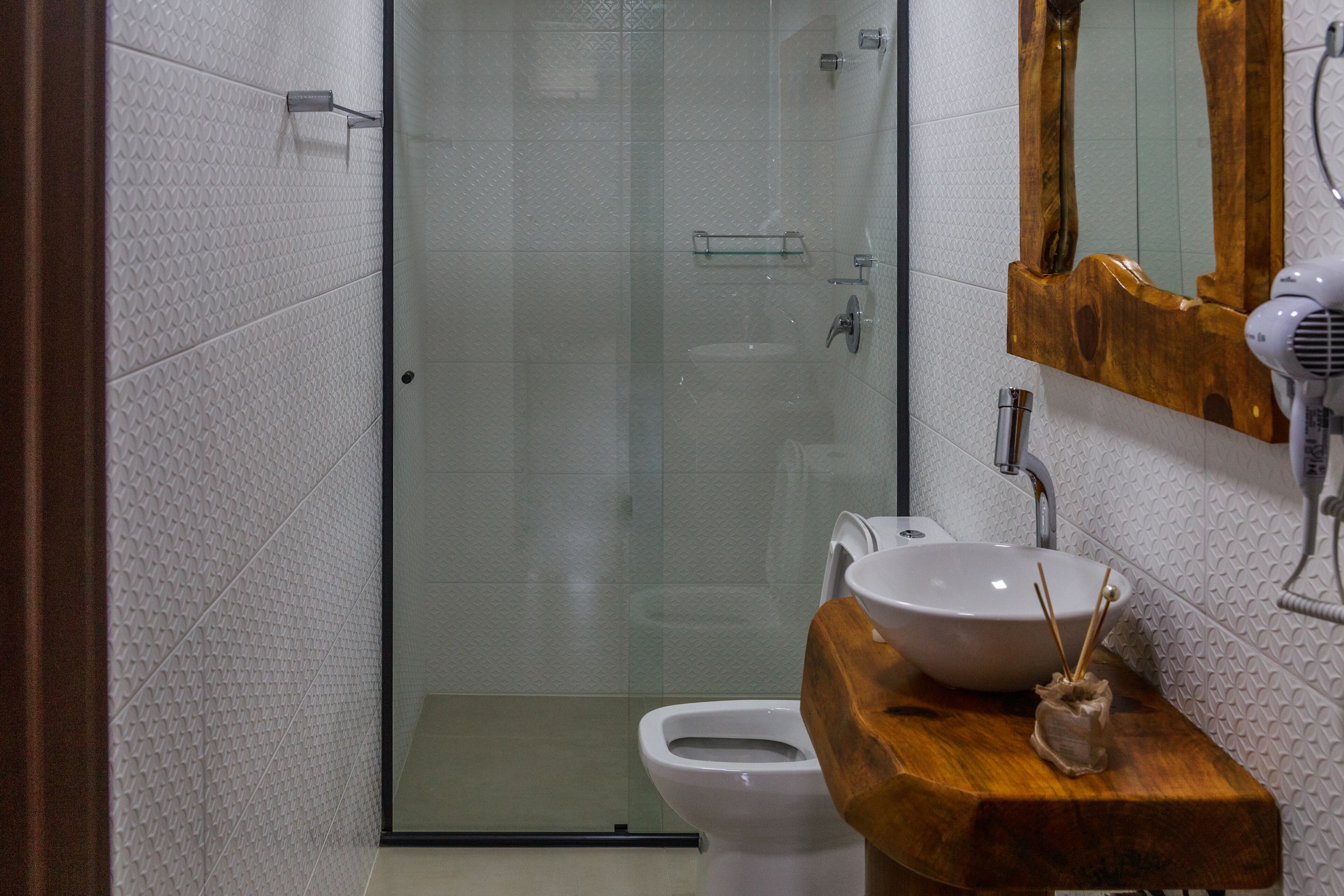 Un baño con cabina de ducha de vidrio, tocador de madera con lavamanos blanco y espejo con marco de madera.