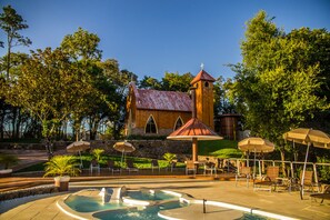 A wooden church with a bell tower, surrounded by a swimming pool and outdoor seating.
