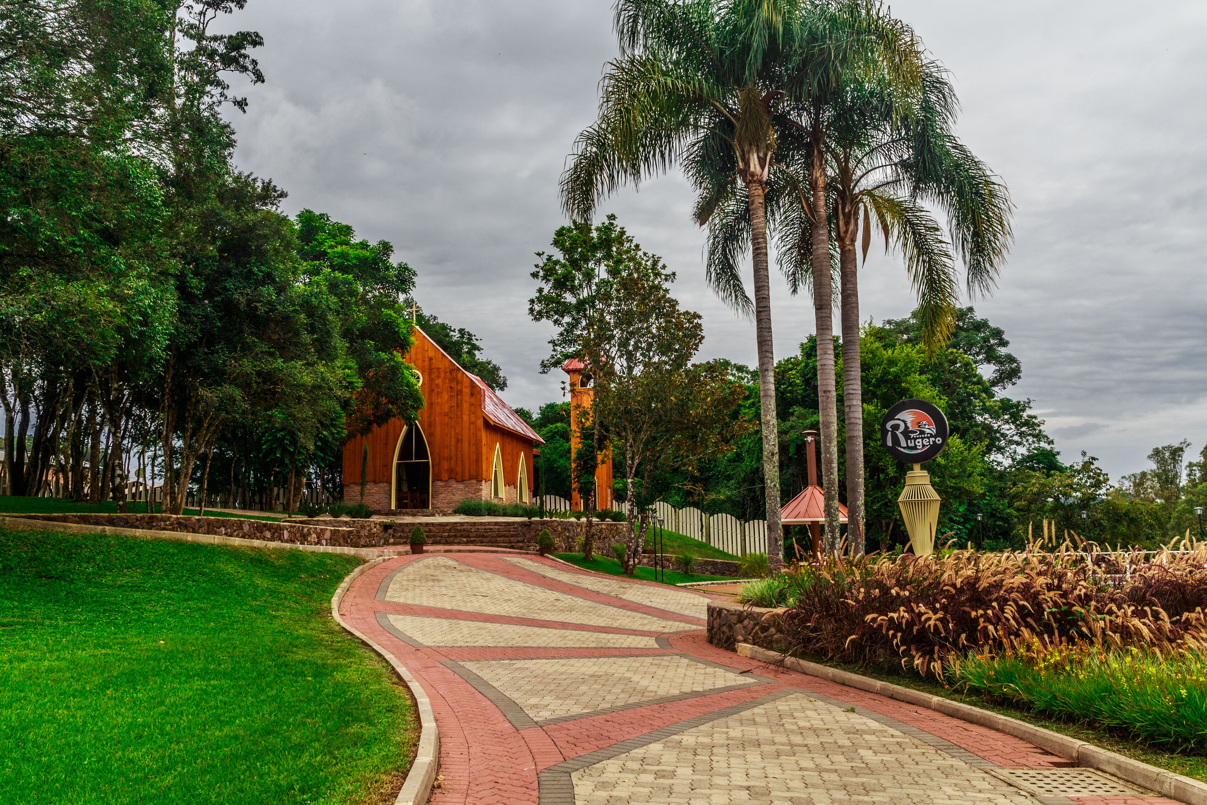 A church with a red roof and a white fence, surrounded by lush greenery and palm trees.