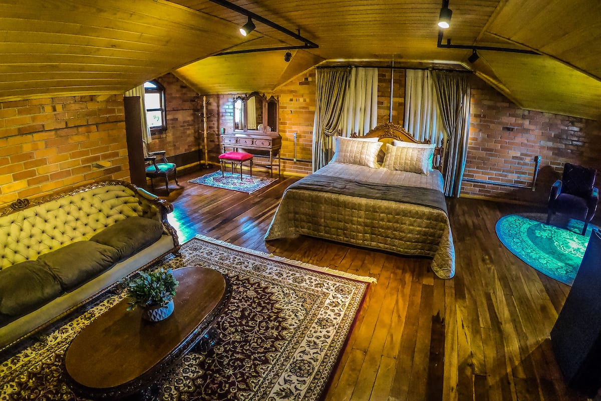 A cozy attic bedroom with a large bed, a sofa, and a small table.