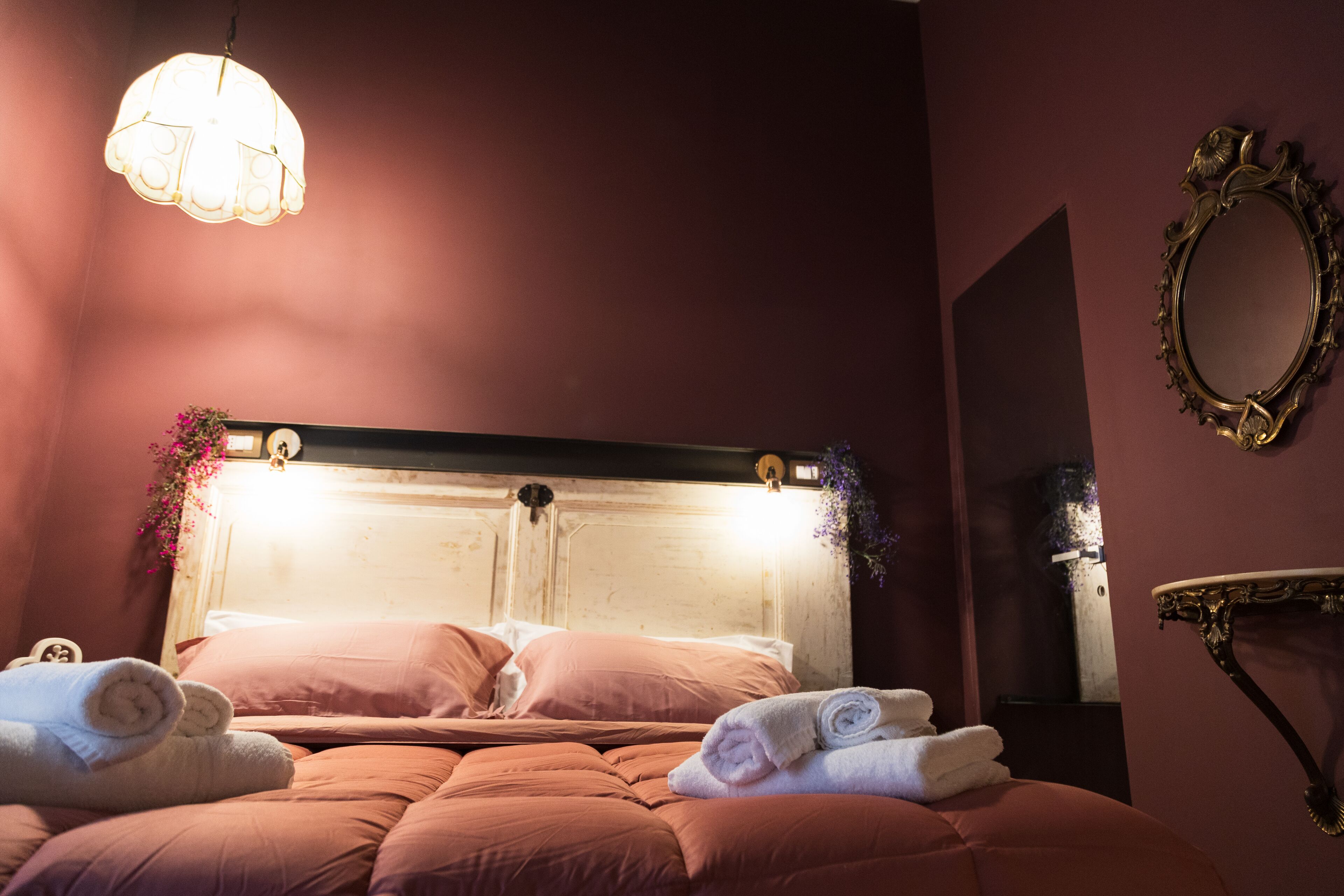 A room with a bed, a mirror, and a wall-mounted light fixture.