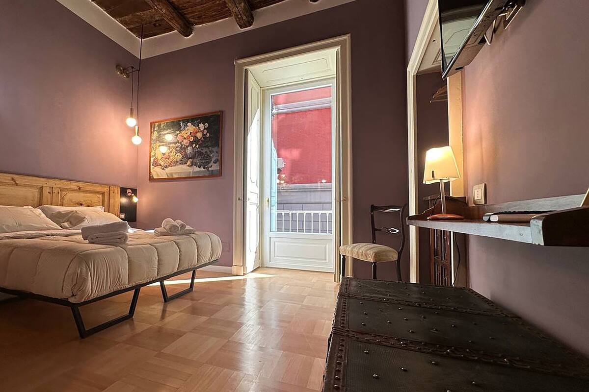 Un dormitorio con cama, mesita de noche, silla y un cuadro en la pared.