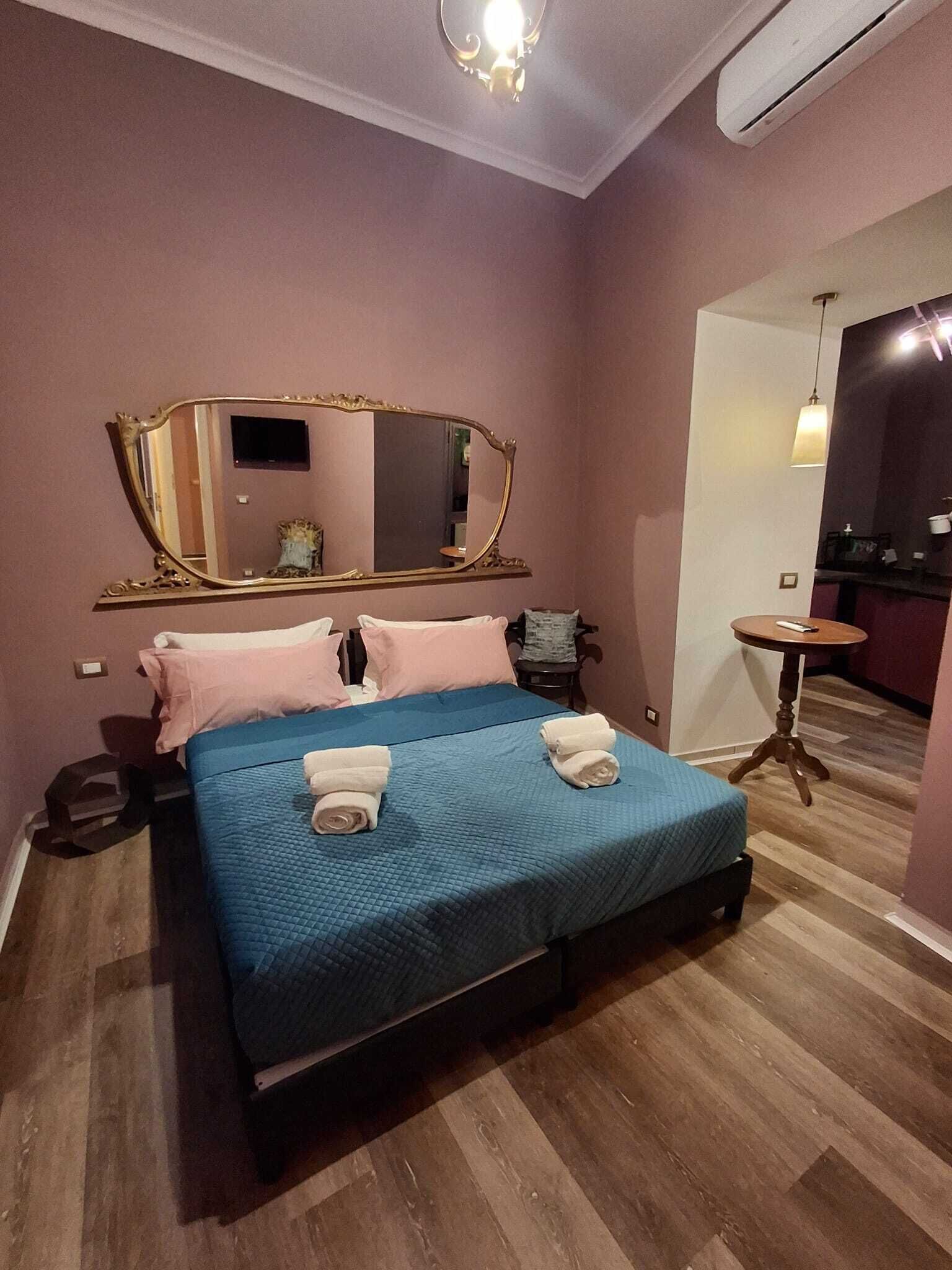 Une chambre avec un grand lit, un miroir, une petite table et un coin cuisine.