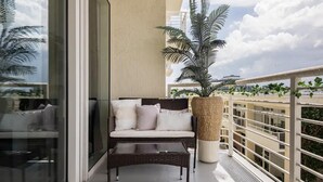 A balcony with a wicker sofa, a coffee table, and a large potted plant.