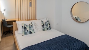 Un dormitorio con cama, escritorio, silla, lámpara colgante y un espejo redondo en la pared.