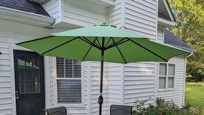 A patio with a round table and four chairs, an umbrella, and a house with white siding and a black door.