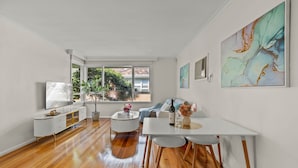 A spacious living area with a white dining table, a sofa, and a TV on a white cabinet. - StayAU 2BRM Beach Family House Hampton (Hampton)