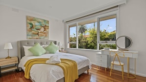 A bedroom with a bed, a desk, a chair, a window, and a painting on the wall. - StayAU 2BRM Beach Family House Hampton (Hampton)
