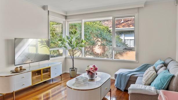 A modern living room with a large TV, a white console table, a sofa, and a window with a view of trees and a building. - StayAU 2BRM Beach Family House Hampton (Hampton)