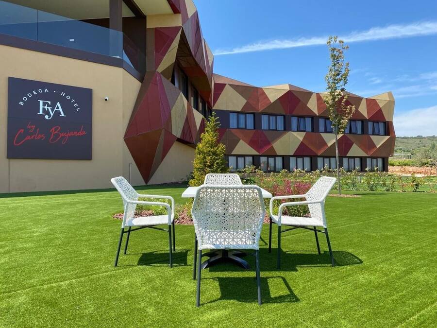 A modern hotel exterior with a geometric facade, a well-maintained lawn, and outdoor seating.
