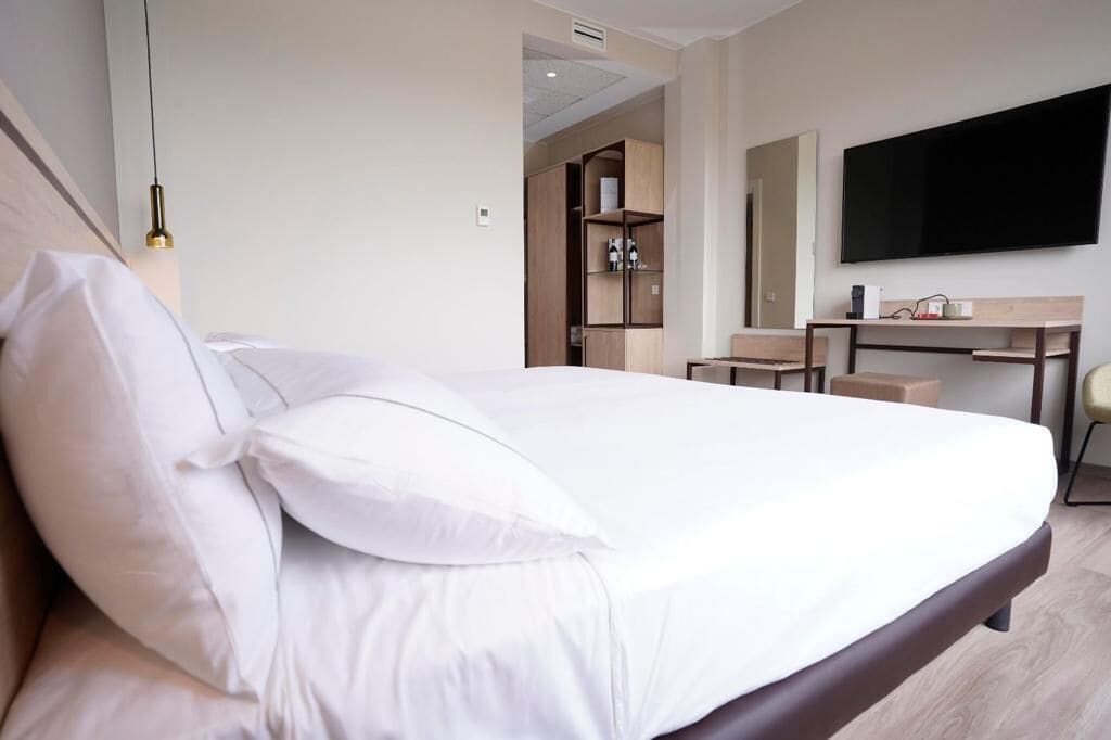 Una habitación de hotel con cama, escritorio, silla, televisor y armario.