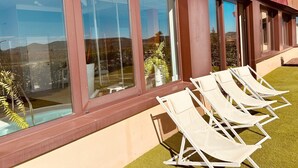 A modern building with large windows and a row of white lounge chairs on a grassy area. - Hotel-Bodegas FyA (Navarrete)