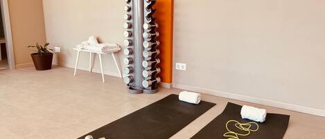 A room with two black exercise mats, a pair of dumbbells, and a jump rope on the floor.