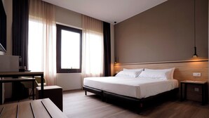 A hotel room with a bed, a desk, a chair, a lamp, and a window with curtains. - Hotel-Bodegas FyA (Navarrete)