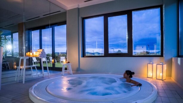 A hot tub in a modern indoor setting with large windows and a view of the cityscape. - Hotel-Bodegas FyA (Navarrete)