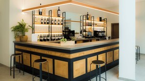 A modern bar area with a wooden counter, multiple wine bottles, and bar stools. - Hotel-Bodegas FyA (Navarrete)