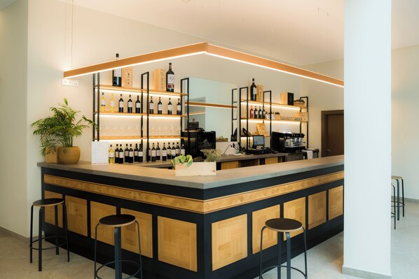 Zona de bar moderna con mostrador de madera, varias botellas de vino y taburetes.