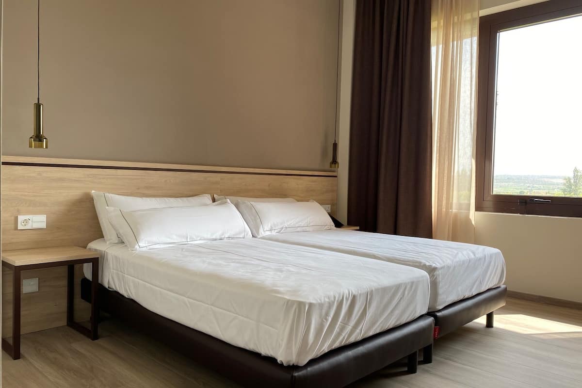 A double bed with a wooden headboard, a bedside table, and a window with curtains.