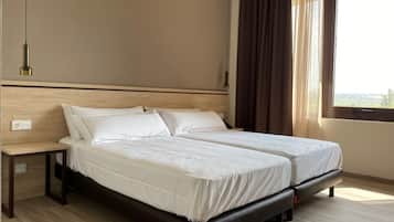 A double bed with a wooden headboard, a bedside table, and a window with curtains.