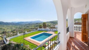 A balcony with a pool overlooking a green landscape and distant hills.