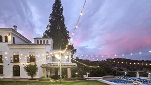 A white building with a balcony, string lights, and a pool area.