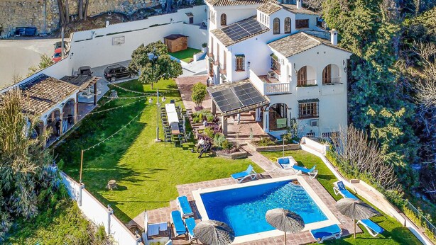 A large, white villa with a swimming pool, multiple balconies, and a well-maintained garden.