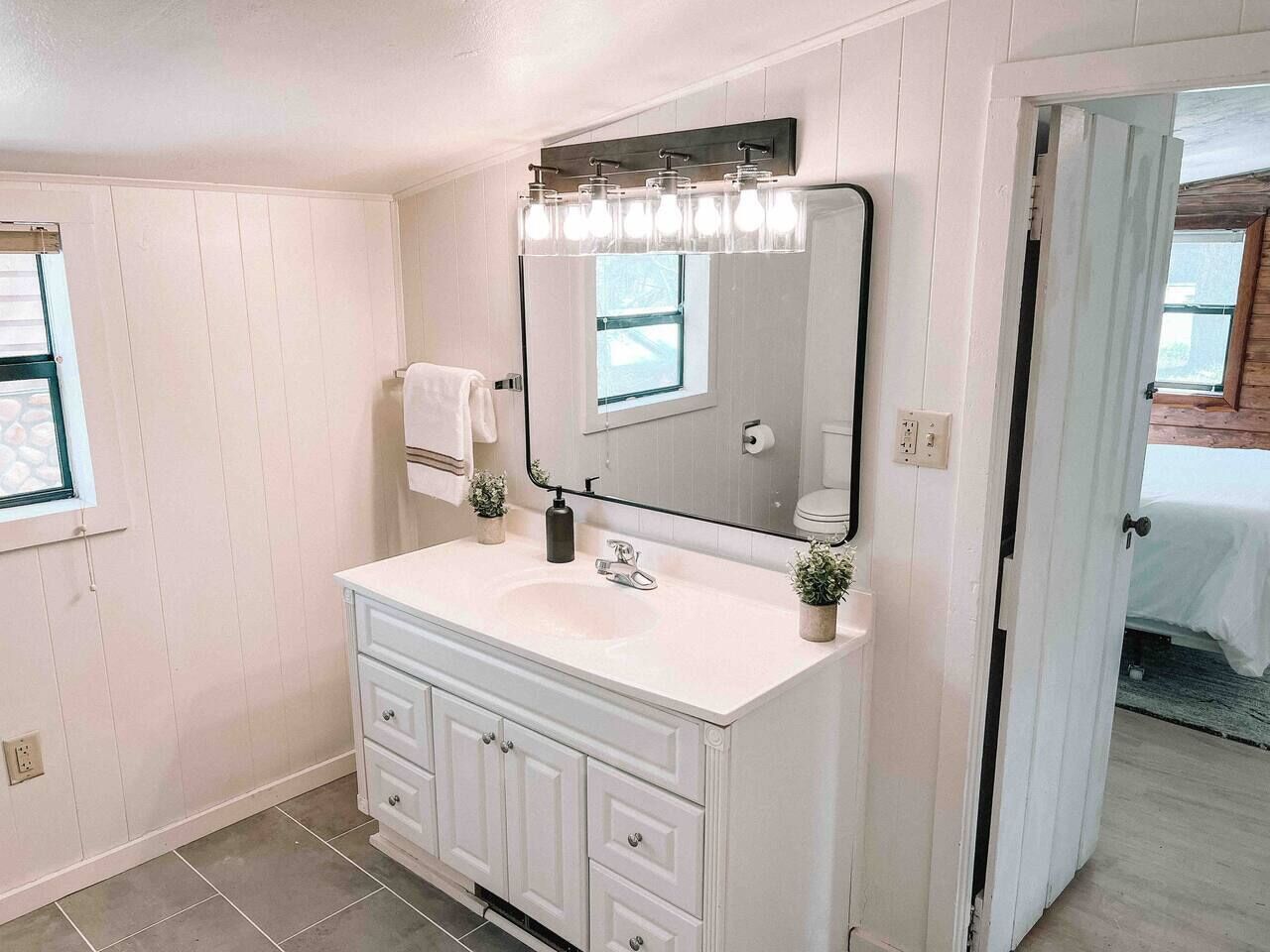 A bathroom with a white vanity, a large mirror, and a light fixture above the mirror.