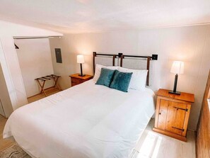 A neatly made bed with white linens, two bedside tables with lamps, and a wooden cabinet.