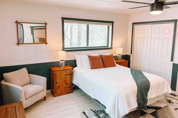 A bedroom with a bed, nightstands, a chair, a window, and a door.