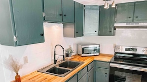 Une cuisine avec des armoires de couleur turquoise, un plan de travail en bois, un four en acier inoxydable et un four à micro-ondes.
