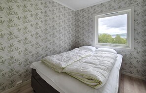 Un dormitorio con cama, ventana y papel tapiz estampado.
