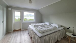 A bedroom with a bed, a window with a view, a door, and a small table with a lamp. - Nice home in Vikebygd with house sea view (Vikebygd)
