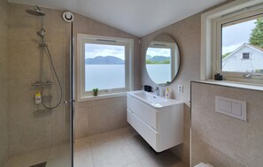 Un baño con ducha, lavamanos, espejo y ventana con vistas a un lago y montañas.