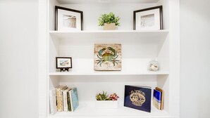 Une étagère blanche, ornée d’œuvres d’art encadrées, d’une plante en pot, d’objets décoratifs et de livres.