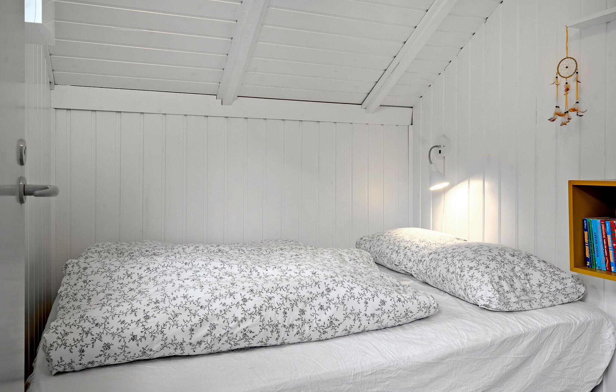 Ein kleines Zimmer mit einem Einzelbett, weißen Wänden und einer schrägen Decke.
