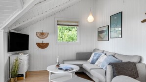 A cozy living room with a flat-screen TV, a round coffee table, a grey sofa, and a window with a view of greenery. - Cozy home in Vestervig with WiFi (Vestervig)