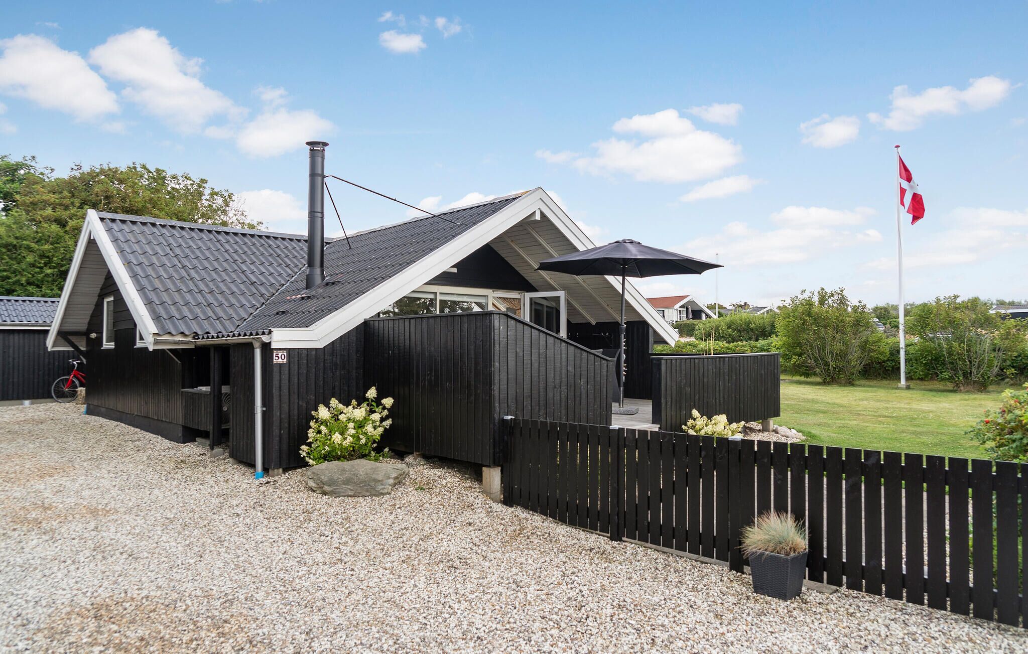 Une maison moderne avec un toit en pente, une cheminée et une clôture noire.