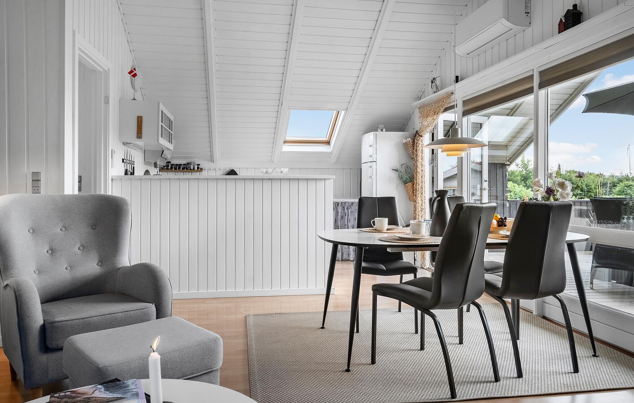 Un intérieur moderne avec un coin repas, un fauteuil gris et une vue dégagée grâce à de grandes fenêtres.