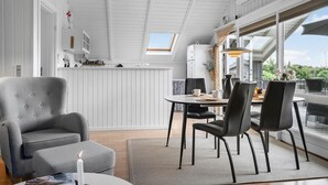 A modern interior with a dining area, a grey armchair, and a view through large windows. - Cozy home in Vestervig with WiFi (Vestervig)