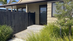 A modern house with a dark wooden fence, a concrete pathway, and green plants.