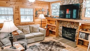 Een gezellig blokhutinterieur met een stenen openhaard, houten wanden, een televisie en een bank.