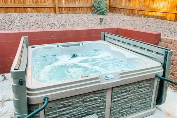 Un jacuzzi con revestimiento de piedra, rodeado por un borde de ladrillo y una valla de madera.