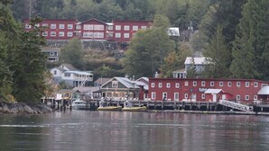 A waterfront property with red buildings, docked boats, and a forested hillside.