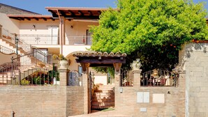 A two-story building with a stone facade, a wooden staircase, and a large tree in front.